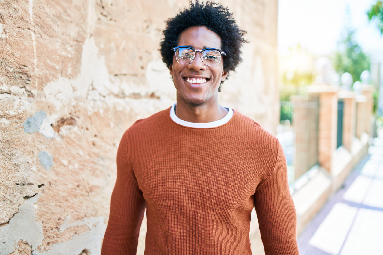 Young handsome african american man wearing casual clothes and glasses smiling happy. Standing with smile on face looking to the camera walking at town street.